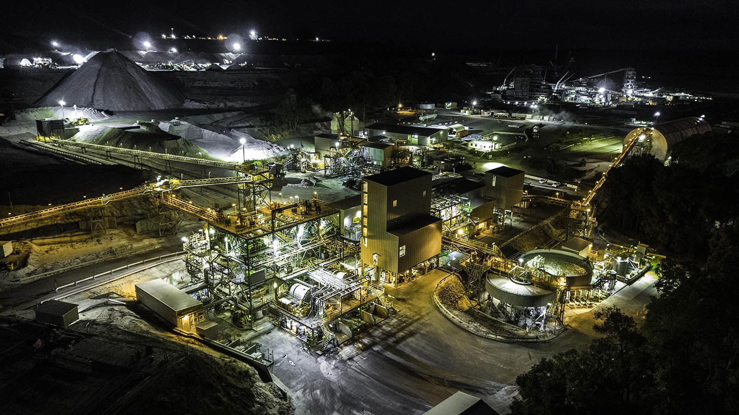 Aerial view of a coal mine illuminated at night, showcasing machinery and mining structures against a dark landscape.
